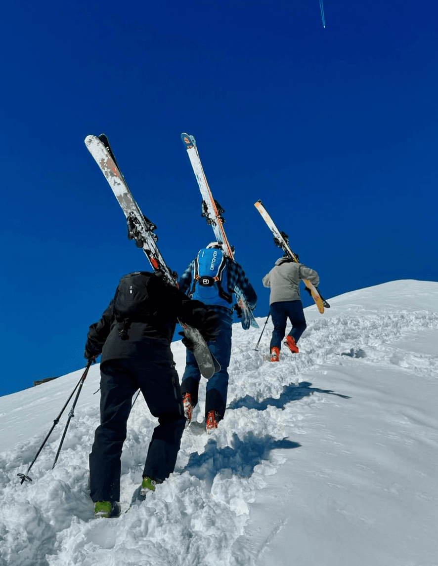 Skiers bootpacking uphill under a deep blue sky